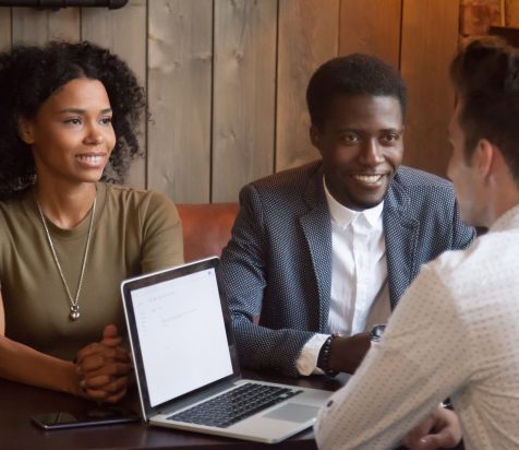 Caucasian realtor or broker consulting millennial African American couple explaining agreement conditions during meeting in coffee shop, white manager talking to black candidates at cafe interview